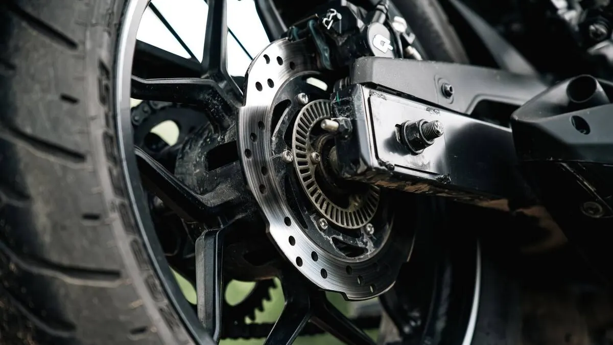 Motard purgeant le frein avant de sa moto, seringue et bocal de liquide dans un atelier